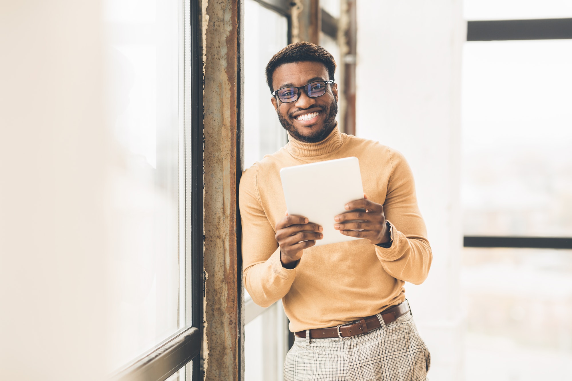 Smiling afro businessman using tablet near office window